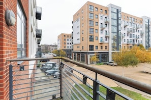 A multi-story residential building with a brick facade, balconies, and a parking area in front.