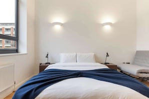 A bedroom with a bed, bedside tables, a chair, and two wall-mounted lights.
