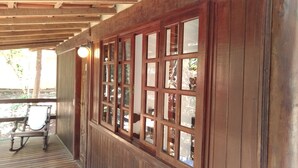 A wooden porch with a table and chairs, large windows, and a ceiling with wooden beams. - Pousada Happiness - Ferradura (Búzios)