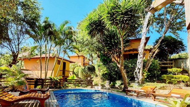 A pool area with wooden loungers, a wooden deck, and tropical vegetation. - Pousada Happiness - Ferradura (Búzios)