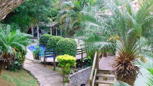 A lush garden with palm trees, a stone pathway, and a pool area. - Pousada Happiness - Ferradura (Búzios)
