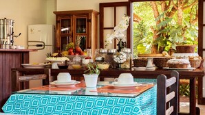 A dining area with a table set for two, a refrigerator, and a cabinet with glass doors. - Pousada Happiness - Ferradura (Búzios)