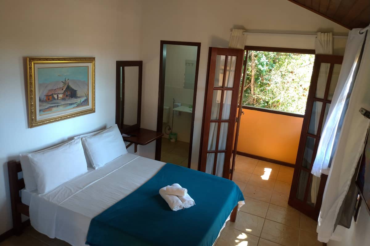 Ein Schlafzimmer mit einem Bett, einem Bild, einem Spiegel und Blick ins Freie.