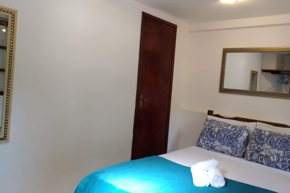 Ein Schlafzimmer mit einem Bett, einer Holztür, einem Spiegel und einer Wandleuchte.