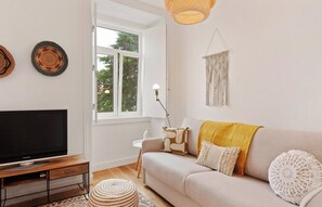 A living room with a sofa, a television, a window, and a lamp. - Modern 1BDR Stay in Charming Belém (Lisboa)
