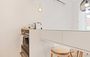 A compact kitchen with a built-in oven, a coffee machine, and a hanging light fixture.