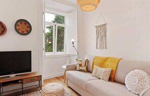 A living room with a television, sofa, and a window with a view of trees.