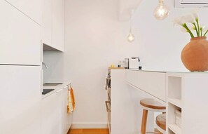 Cocina moderna con armarios blancos, encimera de madera, lámpara colgante y un florero con flores.