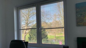 A room with a desk, a chair, a lamp, and a window with blinds. - Ferienwohnung Am Geroweiher (Mönchengladbach)