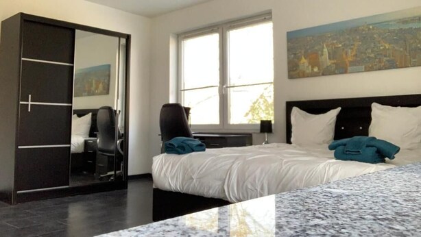 A hotel room with a bed, a desk, a chair, a wardrobe, and a large window. - Ferienwohnung Am Geroweiher (Mönchengladbach)