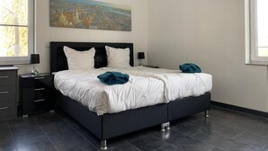 A modern bedroom with a black bed frame, white bedding, and a cityscape painting on the wall. - Ferienwohnung Am Geroweiher (Mönchengladbach)