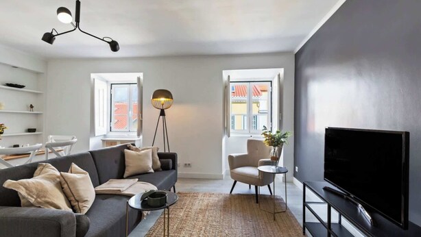 Ein modernes Wohnzimmer mit einer Couch, Fernseher, Stehlampe und Blick ins Freie.