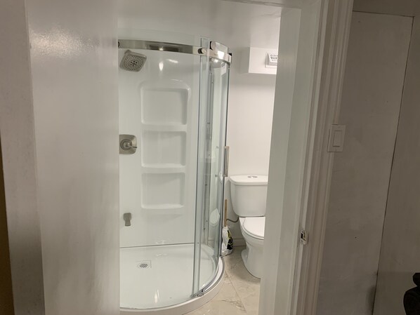 Een badkamer met een douchecabine van glas, een toilet en een vloer betegeld met witte tegels.