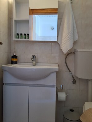 A bathroom with a sink, mirror, and toiletries shelf. - Pension Zoi (Rhodes)