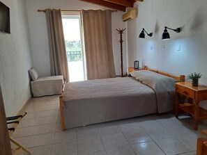 A bedroom with a bed, a bedside table, a lamp, a window with curtains, and a radiator. - Pension Zoi (Rhodes)