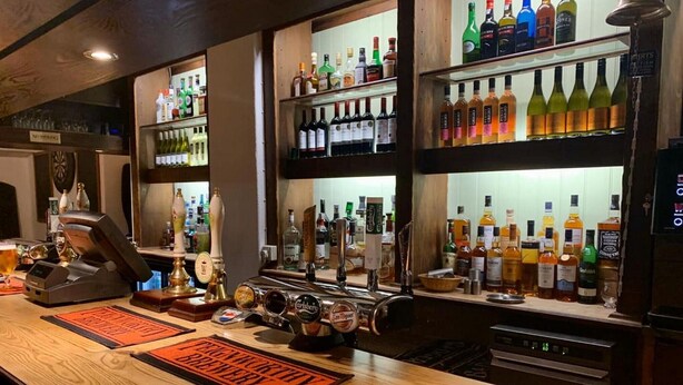 Zona de bar con varias estanterías llenas de botellas de licores, un sistema de grifos y posavasos con el logo de la marca.