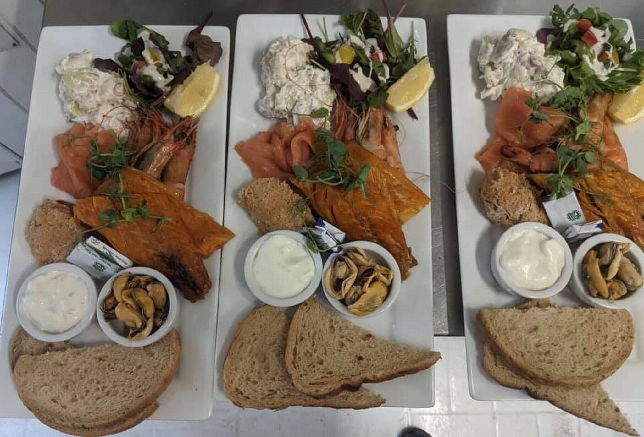 Three plates of food with smoked salmon, bread, and various accompaniments.