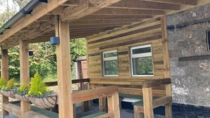 Una estructura de madera con un porche cubierto, bancos y dos ventanas.