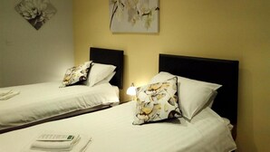 Habitación de hotel con dos camas, cada una con cabecero negro y ropa de cama blanca. Hay una obra de arte floral en la pared sobre las camas y una lámpara de mesa pequeña entre ellas.