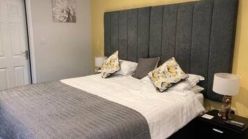 A neatly made bed with a grey and white patterned bedspread, two pillows with a floral design, and a grey upholstered headboard.