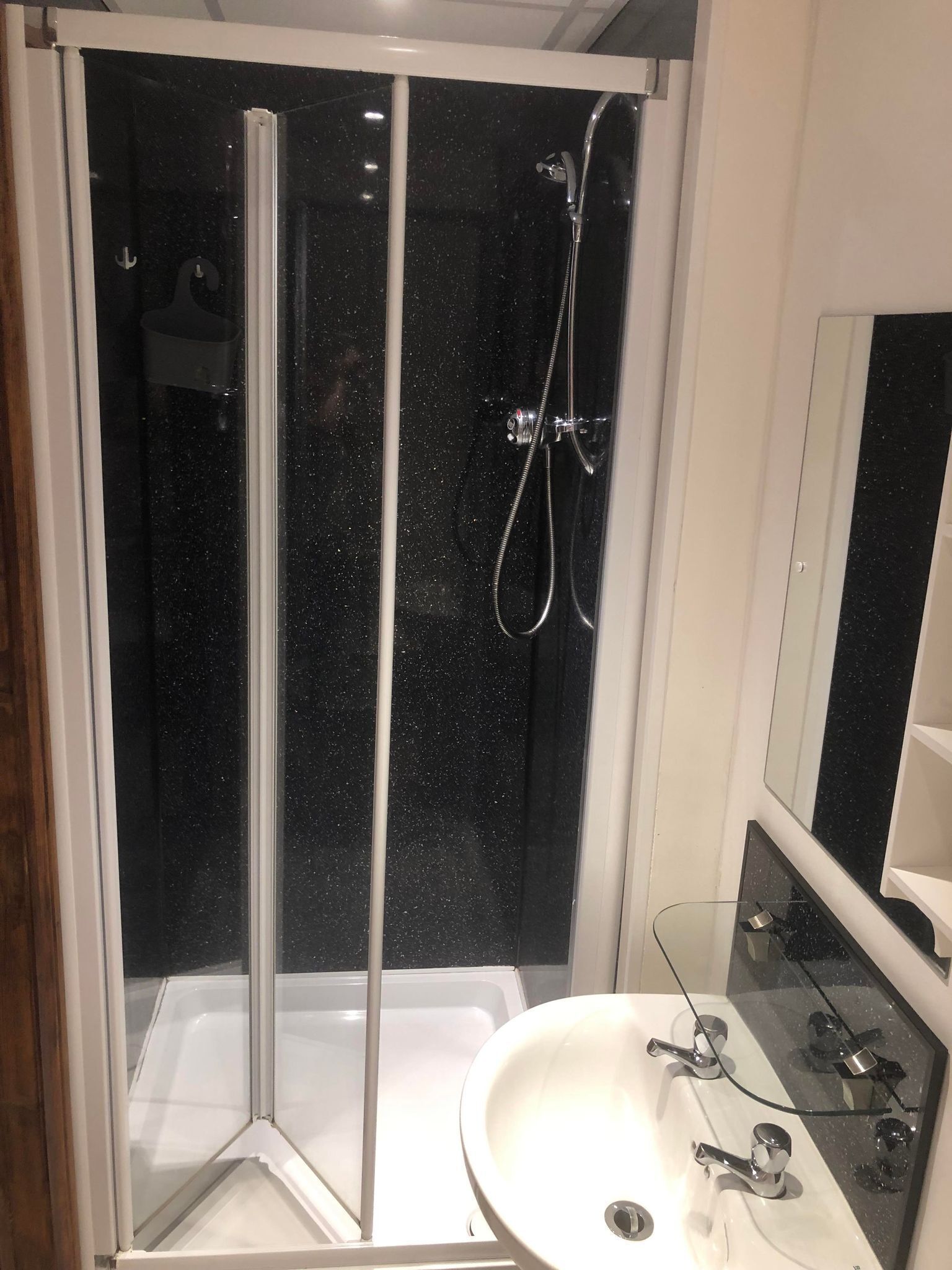 Un baño moderno con ducha de vidrio, lavamanos blanco y espejo.