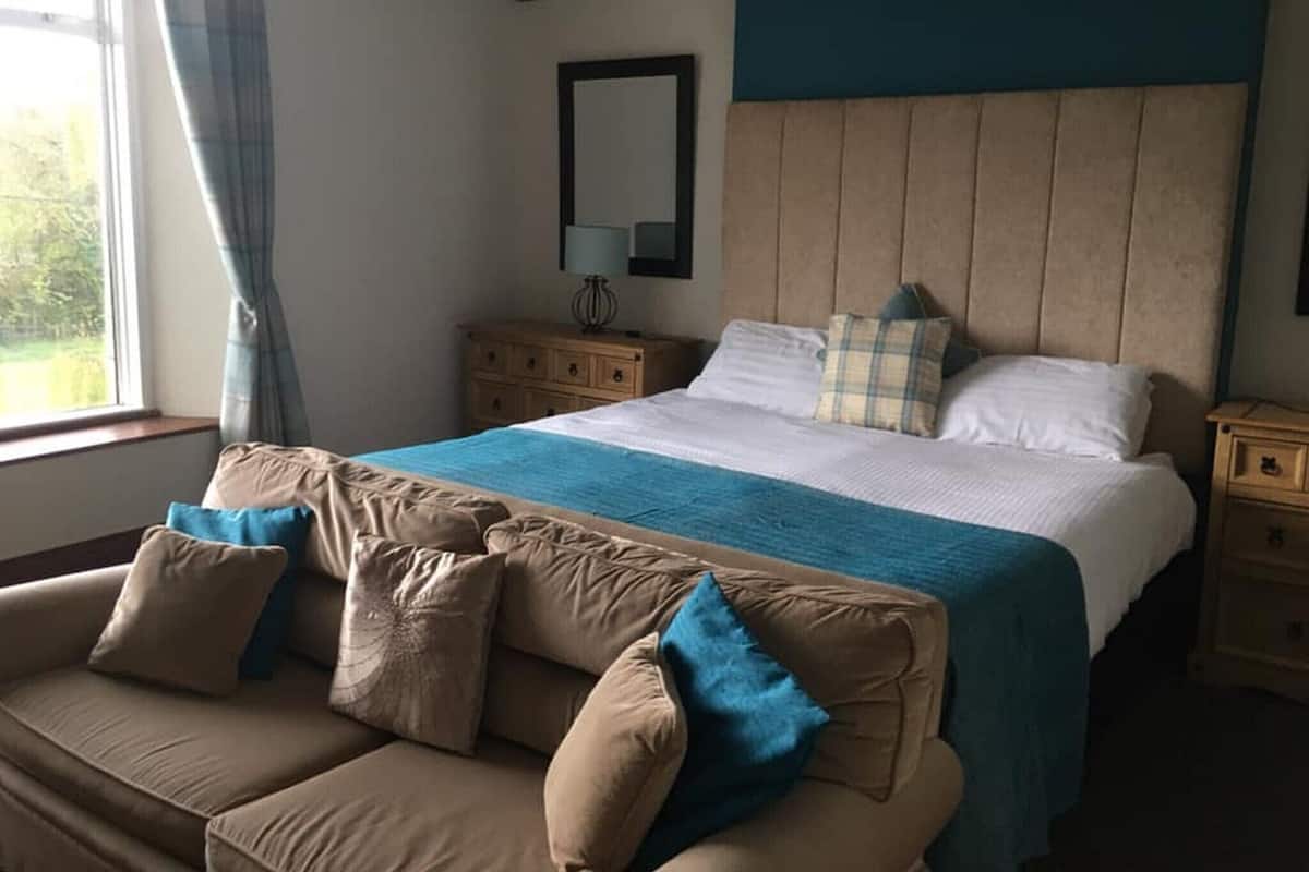 Une chambre à coucher comprenant un lit, une table de chevet, une commode, une fenêtre avec des rideaux et un canapé.