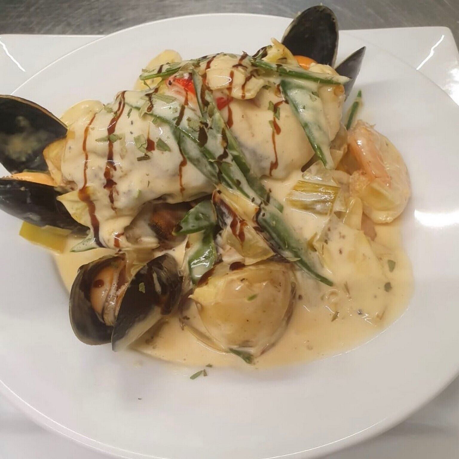 Un plat de fruits de mer composé de moules, de crevettes et d’asperges, nappé d’une sauce crémeuse et servi dans une assiette blanche.