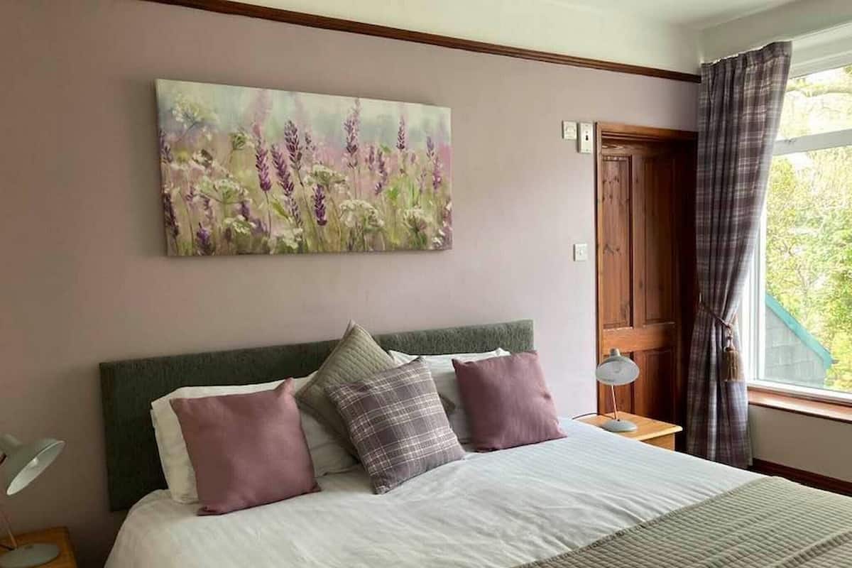 Une chambre à coucher avec un lit, des oreillers, un tableau, une table de chevet et une fenêtre avec des rideaux.