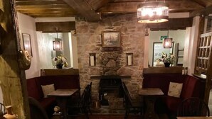 Un interior acogedor con chimenea de piedra, pisos de madera y asientos tapizados en rojo.