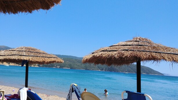 Una playa con sombrillas de paja, un mar azul cristalino y una montaña distante.