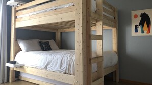 A bunk bed with a wooden frame, white bedding, and a pillow with a quote.