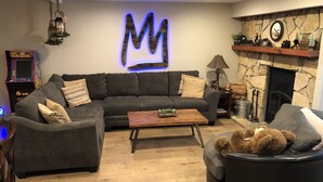 A modern living room with a large 'M' illuminated wall art, a fireplace, and a retro arcade game.