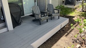 A covered porch with two Adirondack chairs and a grill.