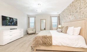 A bedroom with a large bed, a TV mounted on the wall, a chair, and a mirror.