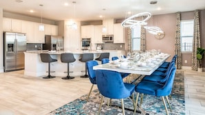 Una cocina moderna con armarios blancos, electrodomésticos de acero inoxidable y una isla central con taburetes de bar.