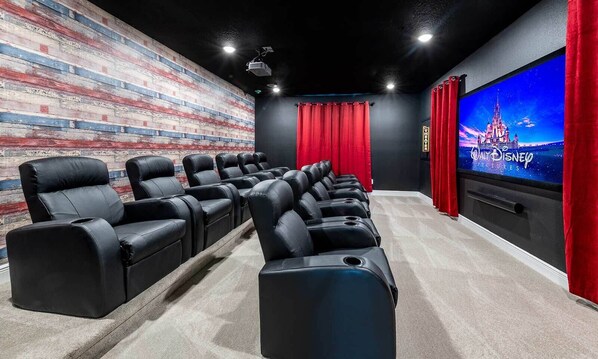 A movie theater with black leather seats, a red curtain, and a large screen displaying 'Walt Disney Pictures'.