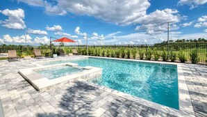 Una piscina rectangular con borde de baldosas, rodeada por una cerca de metal negro y follaje.