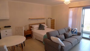 A bedroom with a bed, a sofa, a nightstand, a desk, and a window with curtains. - Neat Modern Studio in Safe Complex in the Heart of Claremont (Cape Town)