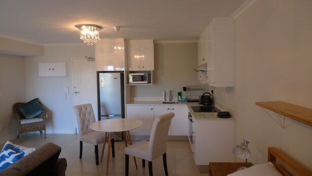A compact living space with a dining area, kitchenette, and a small seating area with a sofa and chairs. - Neat Modern Studio in Safe Complex in the Heart of Claremont (Cape Town)