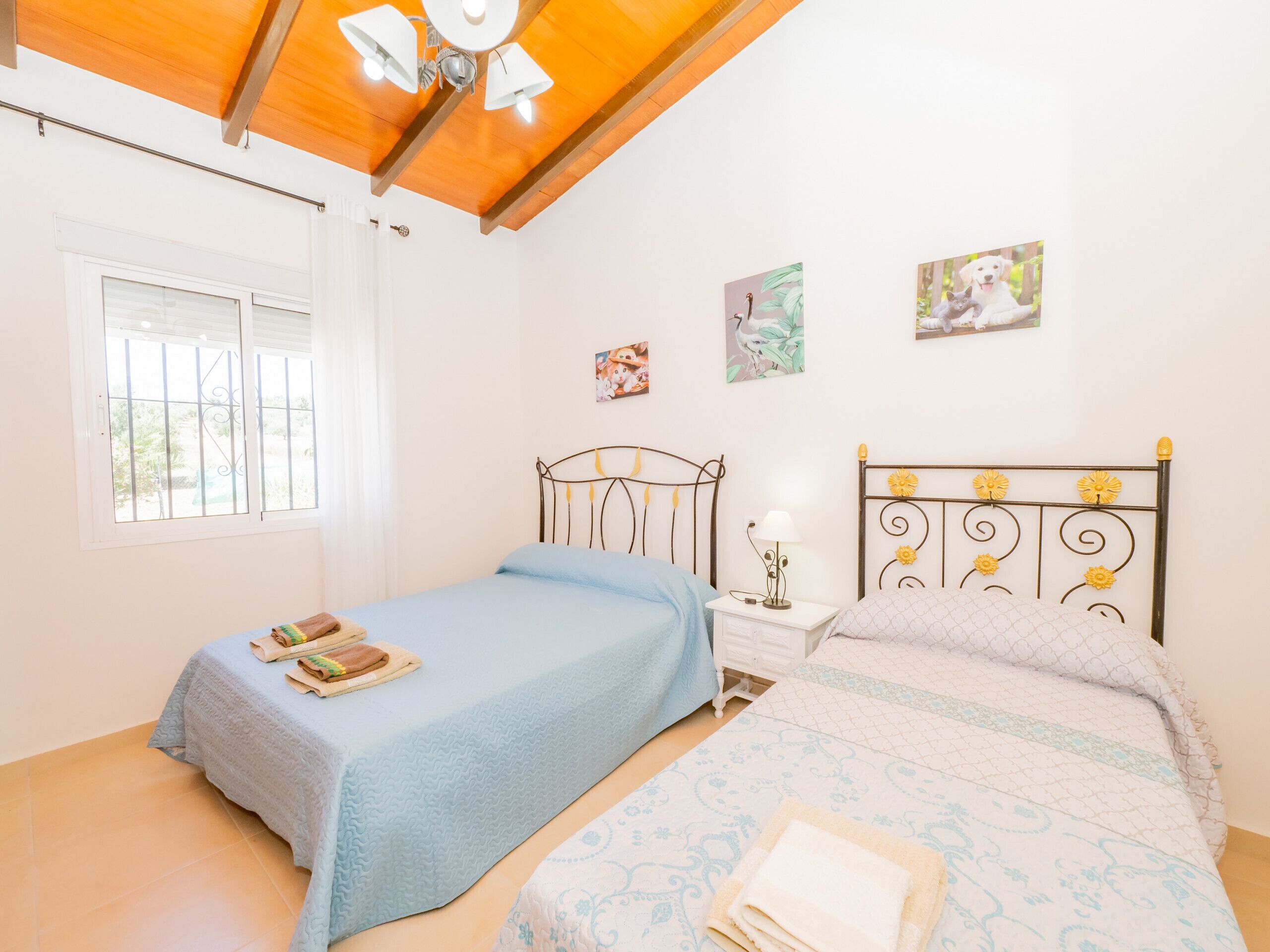 A bedroom with two beds, a window with bars, and a ceiling fan.
