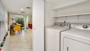 A laundry area with a washing machine and dryer, a dining area with a table and chairs, and a red sofa.