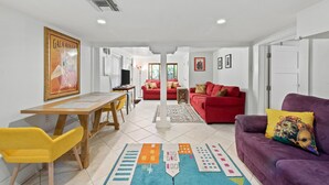 A spacious living area with a wooden dining table, yellow chairs, a red sofa, and a purple sofa with a colorful cushion.