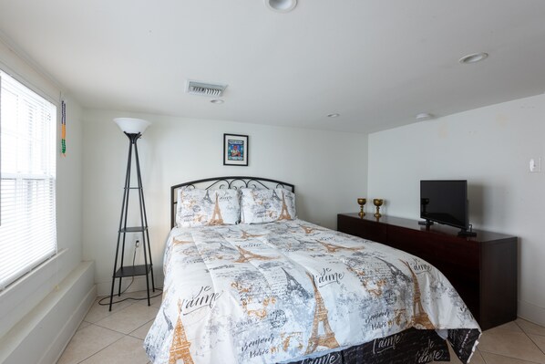 Un dormitorio con cama, lámpara de pie, televisor y un cuadro en la pared.