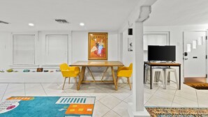 A modern living room with a dining table, yellow chairs, a television, and a colorful rug.
