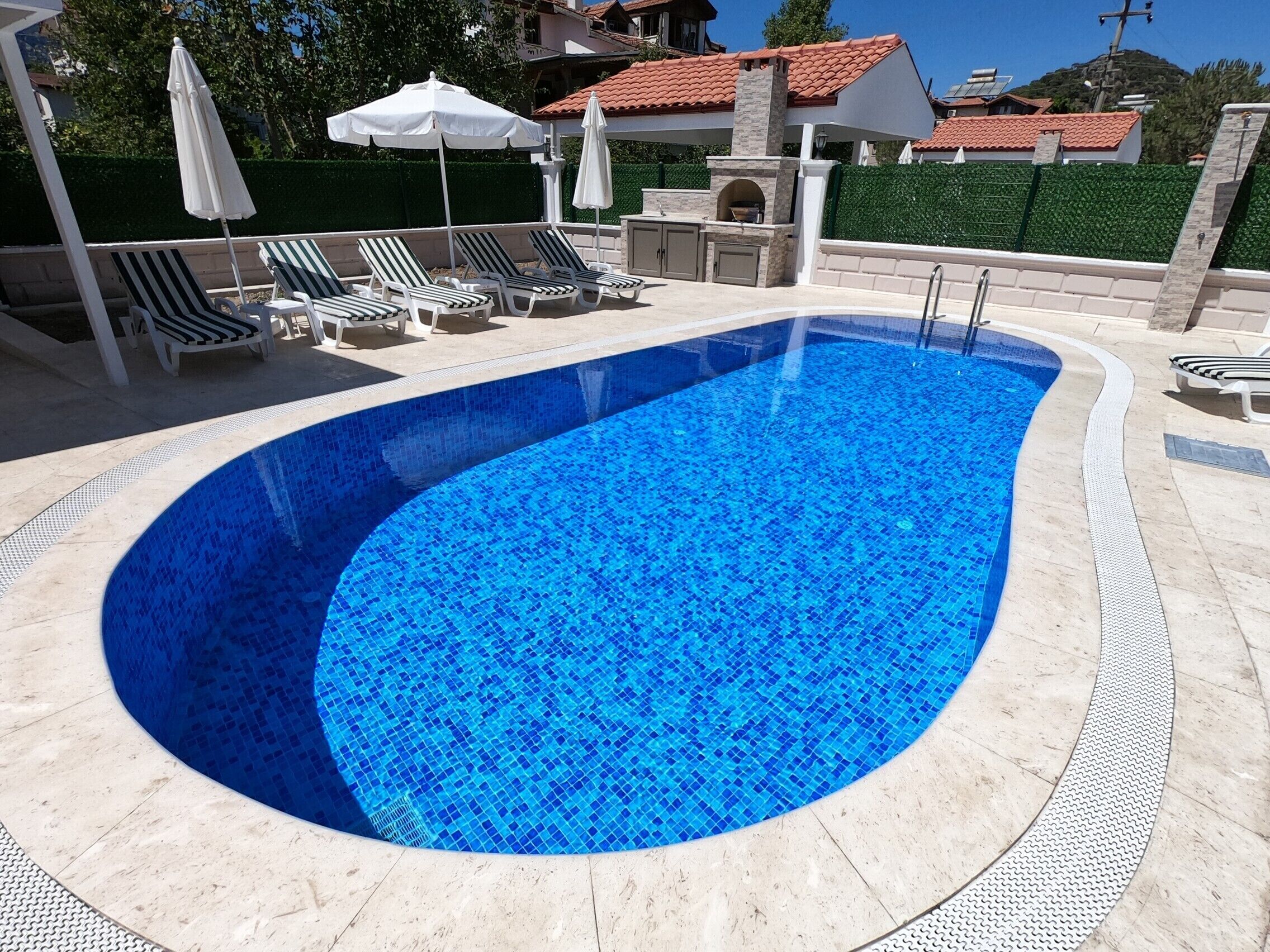 A swimming pool with a tiled edge, lounge chairs, and umbrellas.