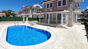 Une maison moderne à deux étages, dotée d’une piscine, d’un patio couvert et offrant une vue sur les maisons voisines.