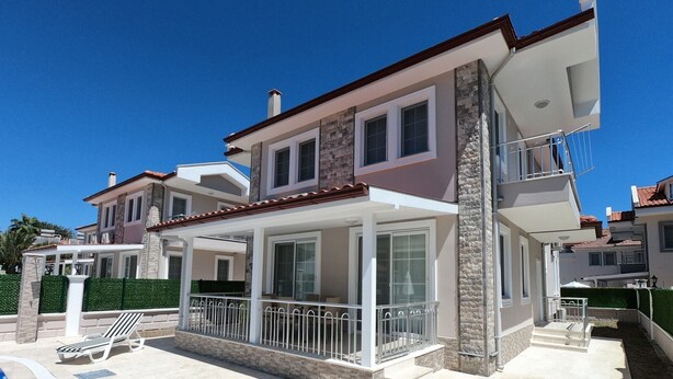 Une maison moderne à deux étages, dotée d’un patio couvert, d’une piscine et d’une façade en pierre.