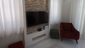 Un salon moderne avec un téléviseur à écran plat fixé à un mur en briques, un fauteuil rouge et un petit pouf.