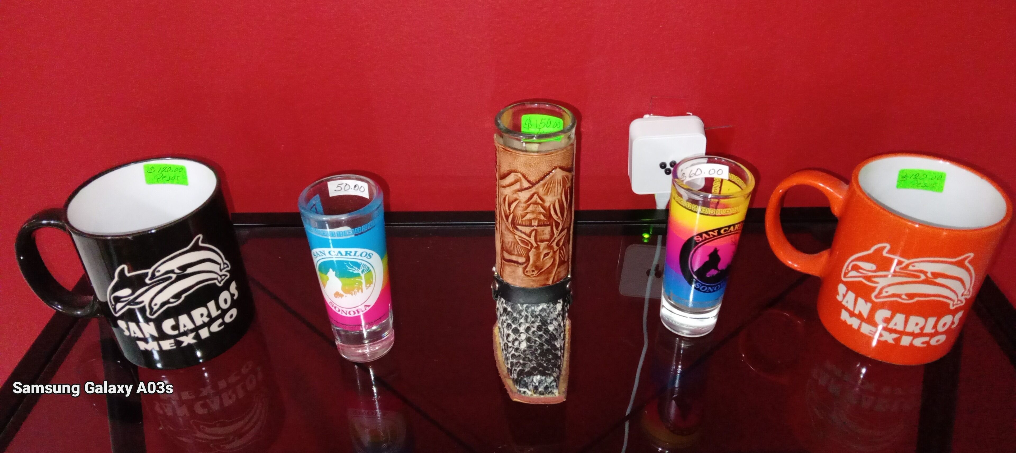 A collection of mugs with various designs and prices displayed on a glass table against a red background.