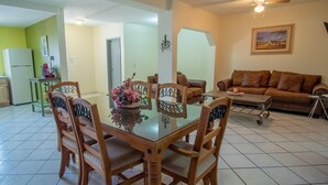 A dining area with a glass-top table, wooden chairs, and a floral centerpiece. There is a brown sofa and a small table with a candle in the living area. - Casa 12-1 - Pet Friendly, Amazing view, and Newly Renovated (San Carlos)